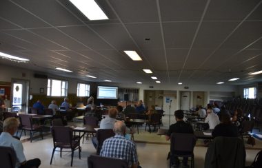 A wide angle shot of a municipal council meeting in a hall with chairs spaced out.