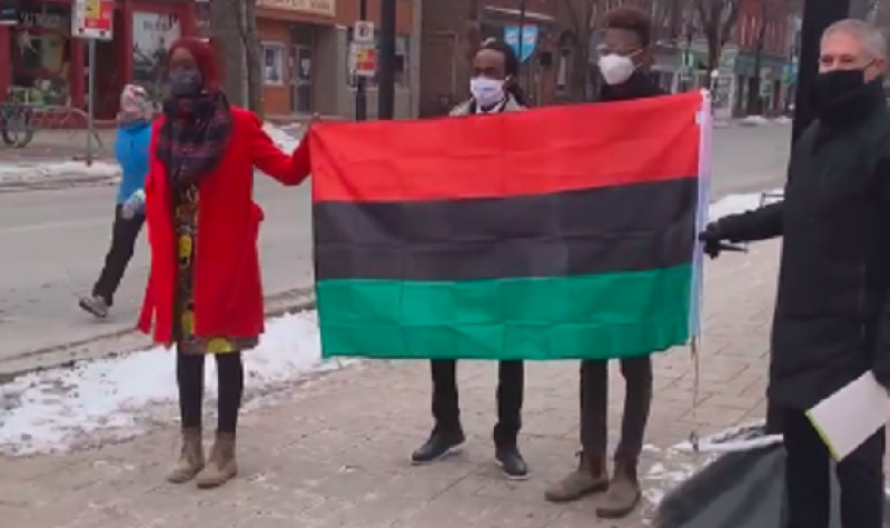 Three Black Lives Matter organizers stand with the Fredericton mayor and hold the Pan-African flag.