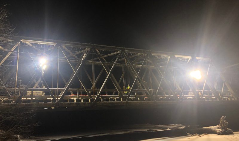 A bridge at night with trouble lights on as engineers and workers assess the damage.