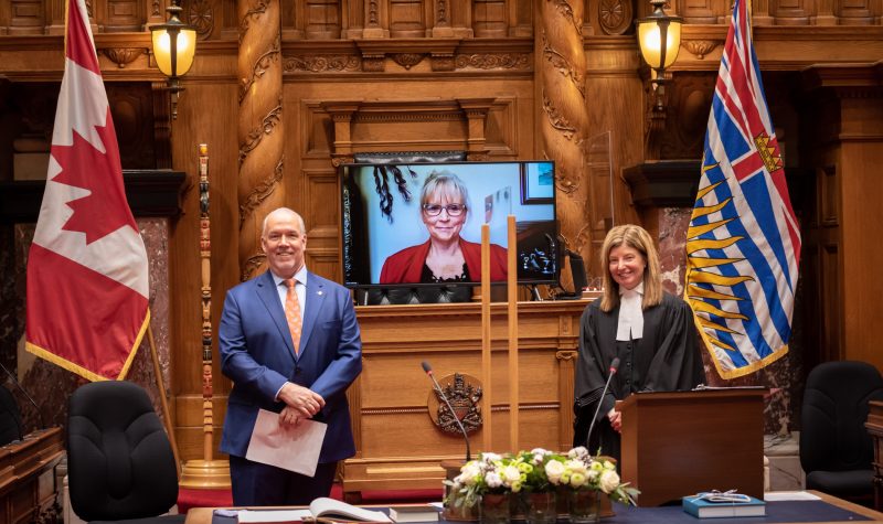 The inside of the BC legislature with the premier and MLA Michele Babchuk on a screen being sworn in virtually.