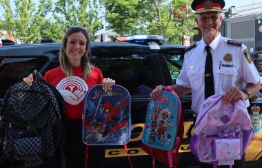 A woman in a red t-shirt and a police officer in uniform showing backpacks that have been collected