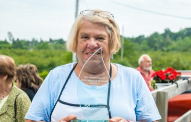 Beverly habillée en bleu clair tient le prix en verre transparent devant elle. Des personnes sont réunies aux alentours