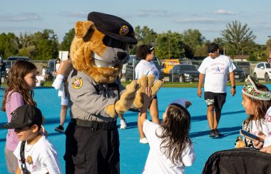 A man dressed as a police dog giving a high five to a child in front of a blue track