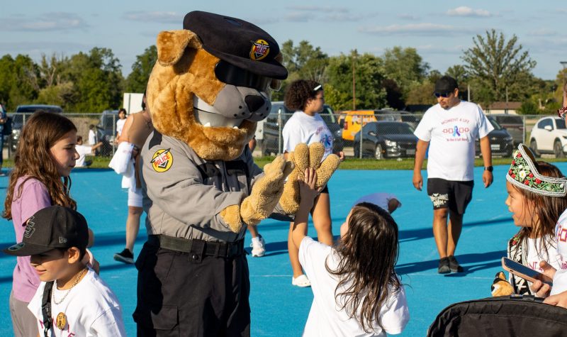 A man dressed as a police dog giving a high five to a child in front of a blue track