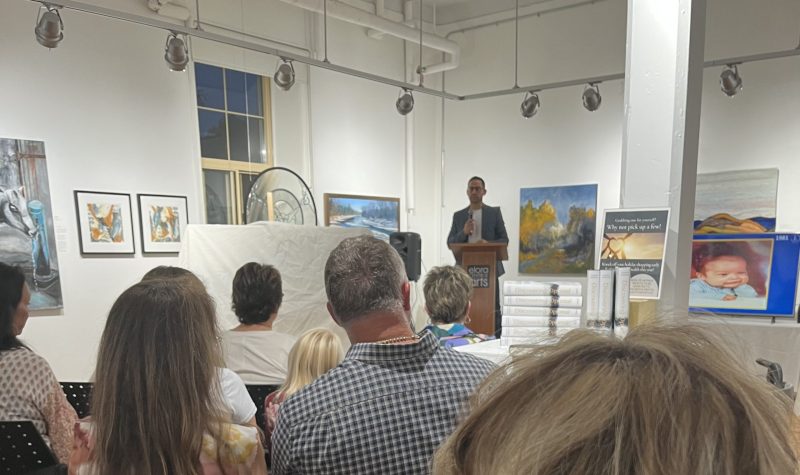 Joseph Gibbons stands before a seated crowd in an art gallery presenting his new book.