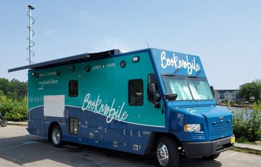 A large blue truck with Bookmobile written along sthe side is parked in front of the ocean