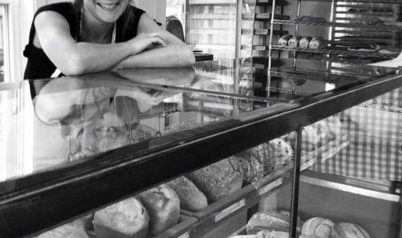 Pictured is Rousseau standing behind her bread counter. You can see a variety of breads through the class windows of the counter.