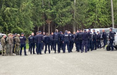 Around 31 RCMP in blue and army green uniform congregate in a forest clearing.