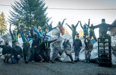 A group of people pose proudly outside in front of a long line of oversized white garbage bags.