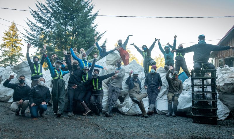 A group of people pose proudly outside in front of a long line of oversized white garbage bags.