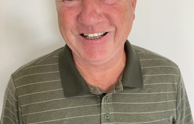 A man smiles in front of a white wall