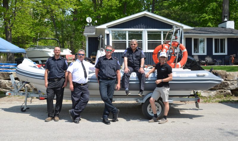 Five men, four of them in firefighter dress uniforms stand in front of a small pontoon boat on a trailer.