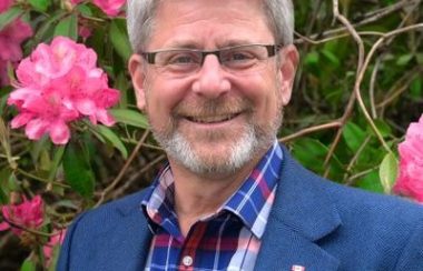 A headshot of Bruce Banman standing against a floral background.