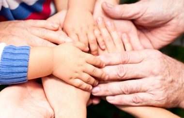 The picture shows a group of hands belonging to adults and children meeting together to represent the need to protect children.