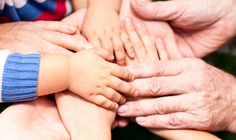 The picture shows a group of hands belonging to adults and children meeting together to represent the need to protect children.