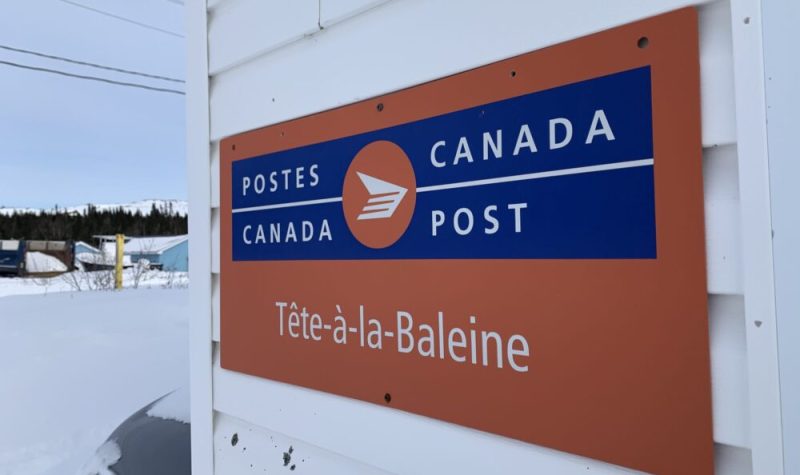 Un panneau aux couleurs de Postes Canada indiquant Tête-à-la-Baleine est accroché sur un mur extérieur.