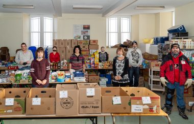 A group of volunteers standing behind tables filled with boxes of goods.
