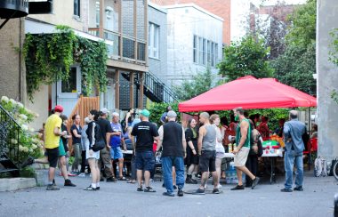 Community members gather in front of tents of food at a community BBQ.