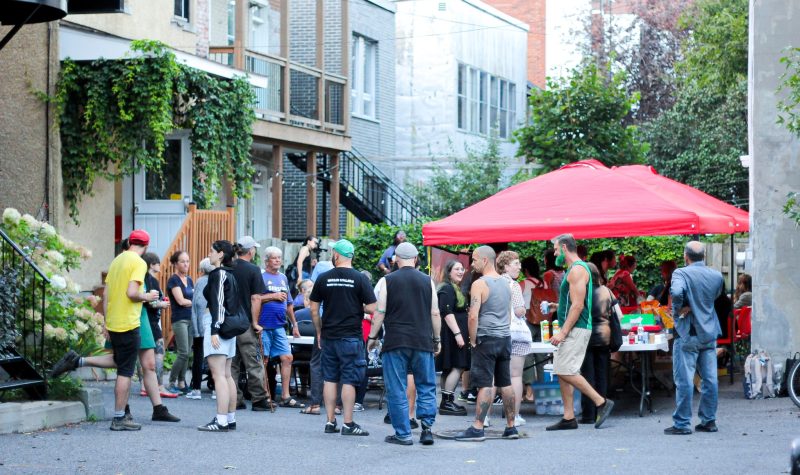 Community members gather in front of tents of food at a community BBQ.