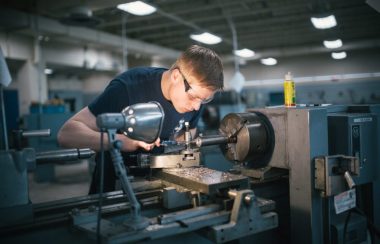 Un jeune homme est penché au-dessus d'une machine qui perce une pièce de métal.