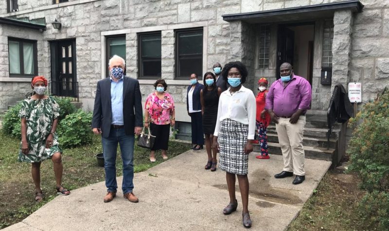 Denis Trudel avec des membres de la communauté noire davant un bâtiment en pierre grise. Les gens portent tous masqués.