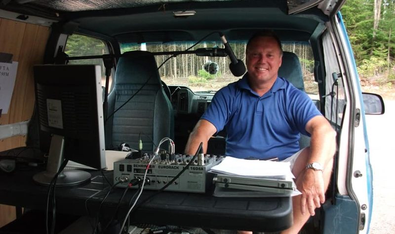 A person sits in the back of a van with a microphone and other equipment.