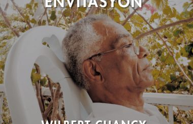 Wilbert Chancy, yeux fermés et lunettes, cheveux grisonnants, assis dans son jardin à Jacmel