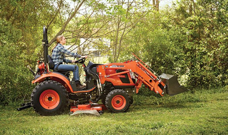 Photo of a man driving a small orange tractor with a shovel on the front.