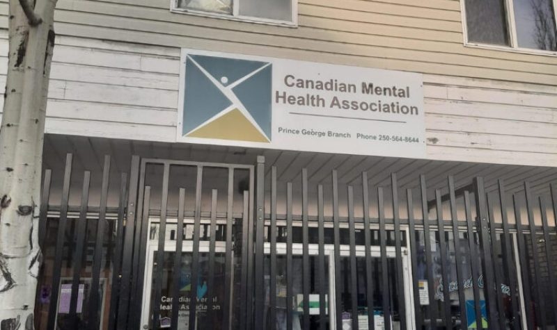 The image shows a barred store front with a sign for the Canadian Mental Health Association, Prince George branch.