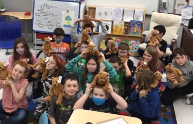 A group of elementary school kids hold identical teddy bears and smile.