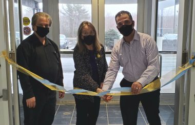 Three people stand in a doorway prepaing to cut a ceremonial ribbon