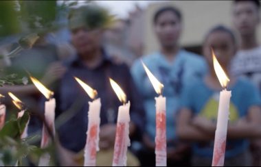 Ignited candles stand in front of a group of people in the background.