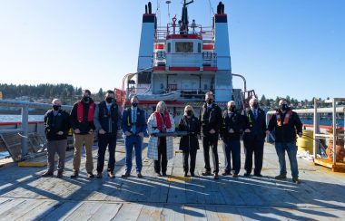 A row of people pose in front of an industrial ship.