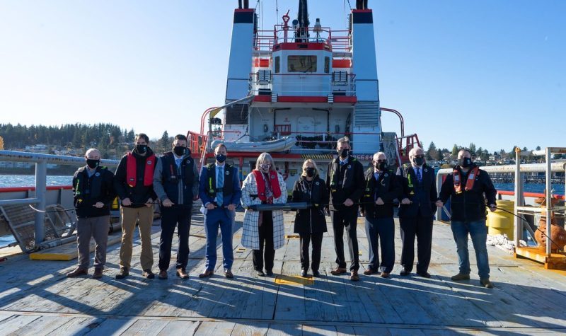 A row of people pose in front of an industrial ship.