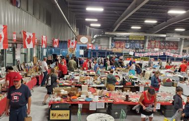 A crowded market set up inside an arena, with Canadian flags decorating the walls.