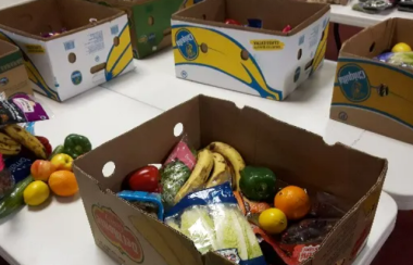 Des boites de cartons remplies de fruits et de légumes sur une table blanche.