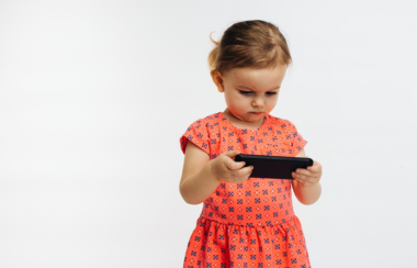 Une petite fille tient fixement un smartphone dont l'image la captive