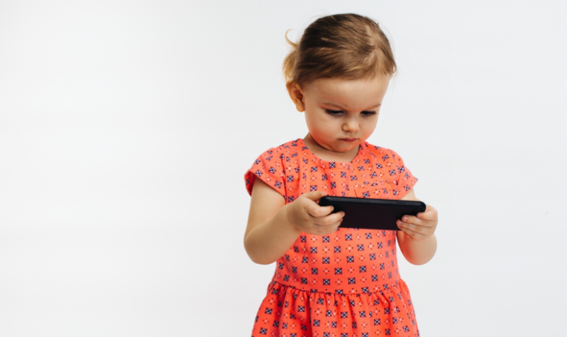 Une petite fille tient fixement un smartphone dont l'image la captive