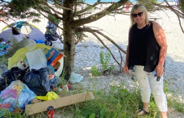 A photo of Queens-Shelburne MLA Kim Masland stands next to a pile of garbage at Carters Beach.