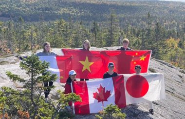 Five young people stand atop a hill displaying their country's flags