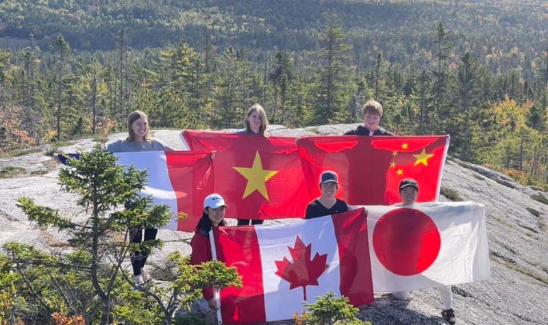 Five young people stand atop a hill displaying their country's flags