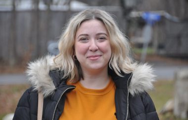 A headshot of Pontiac NDP riding association president Catherine Emond-Provencher, standing outdoors wearing a black parka and an orange shirt.