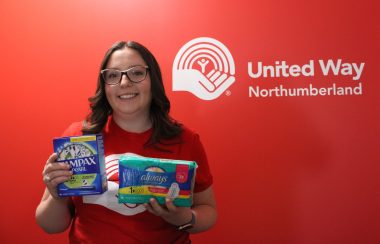 A woman stands against a red background for United Way displaying menstrual products