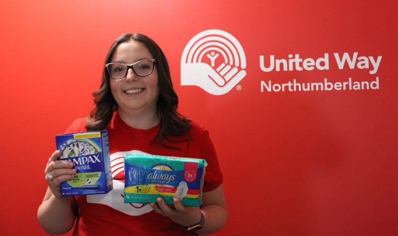 A woman stands against a red background for United Way displaying menstrual products