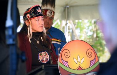 A Wolastoqey chief, wearing traditional attire, speaking at a podium.