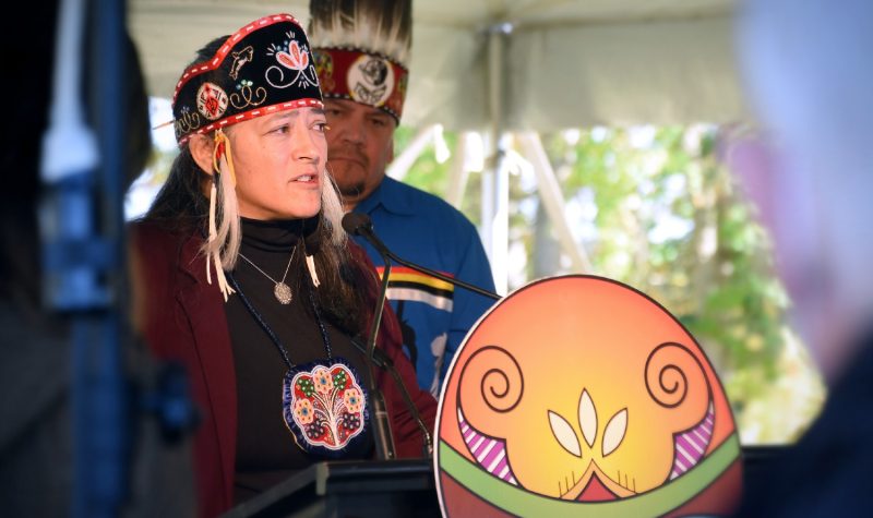 A Wolastoqey chief, wearing traditional attire, speaking at a podium.