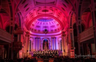 Les choristes chantent dans l'église de La Prairie dont le plafond est illuminé en rose et rouge