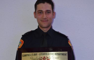 A young man dressed in a formal firefighter outfit holds up a plaque awarded to the Campbell's Bay-Litchfield Firefighter of the Year.