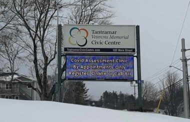 A sign for the Tantramar Veterans Memorial Civic Centre COVID-19 assessment site in a snowy field on an overcast day