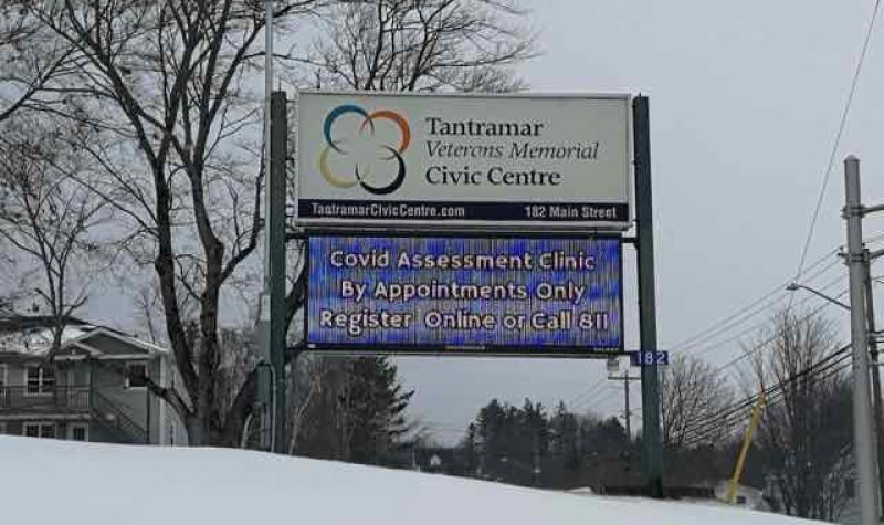 A sign for the Tantramar Veterans Memorial Civic Centre COVID-19 assessment site in a snowy field on an overcast day